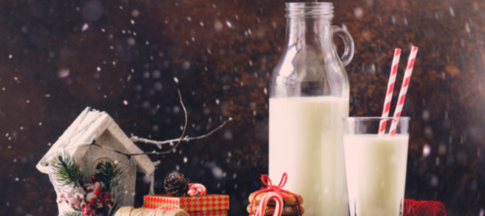 A festive scene of a bottle and glass of milk beside gingerbread biscuits and a gifts