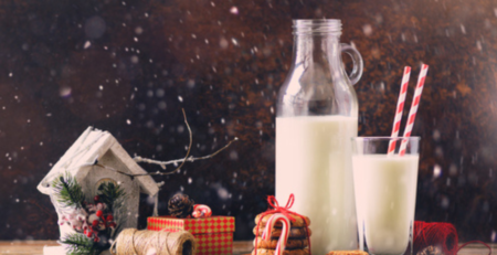 A festive scene of a bottle and glass of milk beside gingerbread biscuits and a gifts