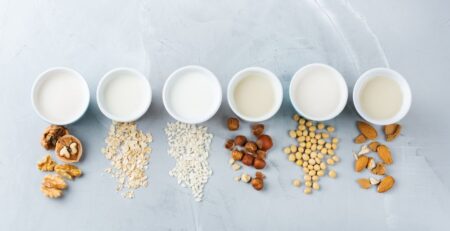 Cups of milk and different kinds of grains they are made from, shown from above