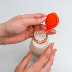 A red Milk Topz bottle cap shown open on a full milk bottle