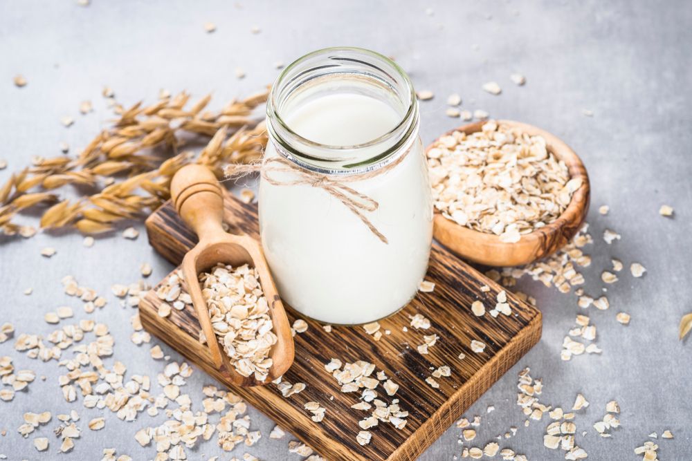 Oat milk in a glass mason jar surrounded by oats and wooden scoopers