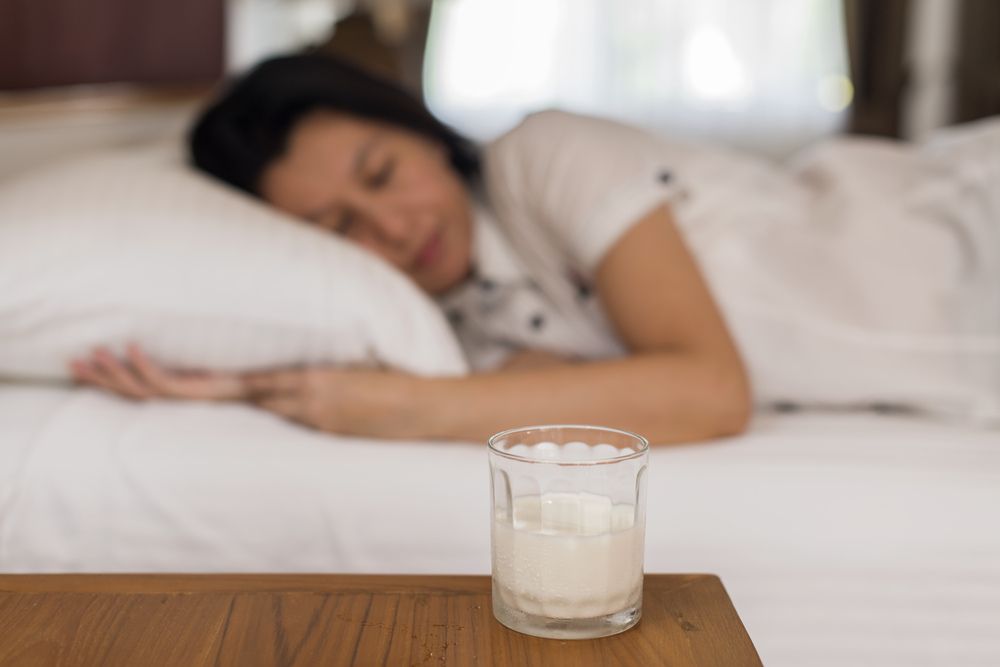 A woman sleeps comfortably in bed, a glass of milk sits on the bedside table